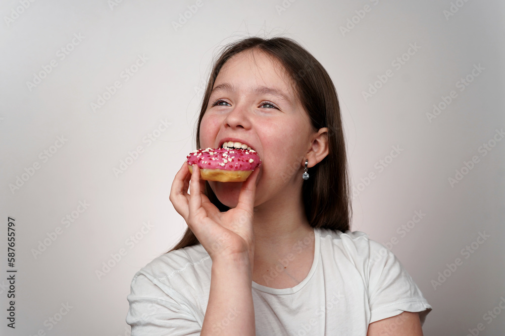 Caucasian Girl in white T-shirt Eating Donut in her hands with pink glaze on white background Caucasian Girl in white T-shirt Eating Donut in her hands with pink glaze on white background