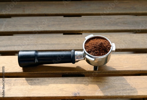 A metal horn of a professional coffee machine filled with brown powder of ground coffee beans stands.