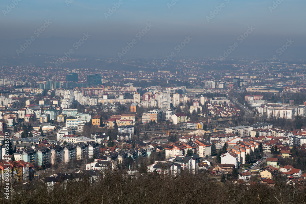 Cityscape of Banja Luka during sunny day, distant hill barely visible in hazy polluted air