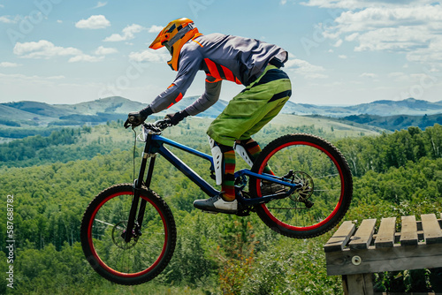 male rider on downhill bike jumping wooden drop, racing DH mountain bike, extreme sport games