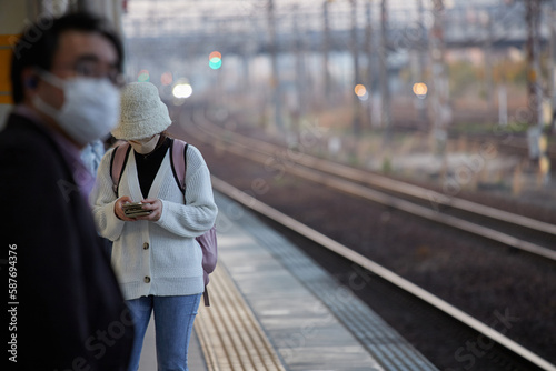 駅のホームで電車を待ちながらスマートフォンを弄る若い女性の姿
