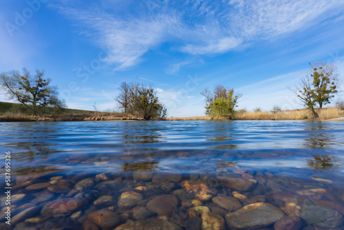 Calm clear lake with sight onto stones underwater and trees in the background photo