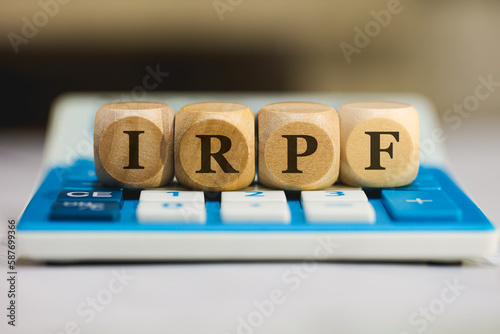 A sigla IRPF de Imposto sobre a Renda das Pessoas Físicas em Português do Brasil escrita em dados de madeira que estão sobre uma calculadora azul. Economia brasileira. photo