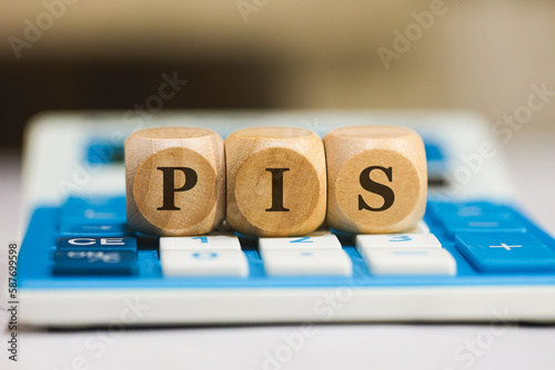 A sigla PIS para Programa de Integração Social escrita em dados de madeira que estão sobre uma calculadora azul. Economia brasileira, imposto, governo brasileiro. photo