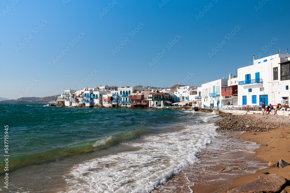 View from the beach the white seaside houses of the village of Chora on the island of Mykonos in Greece. In the background the blue sky during summer vacation.