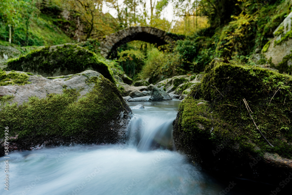 small cascade of water in long exposure in front of an ancient arched stone bridge small cascade of water in long exposure in front of an ancient arched stone bridge