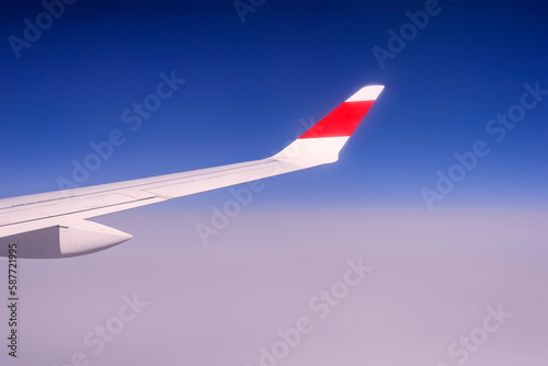 Travel and vacation concept. Wing of an airplane flying above the clouds. Clear blue sky.