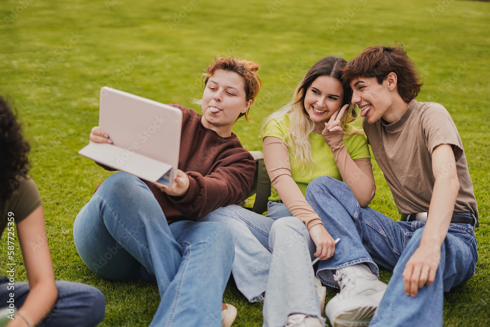 Young students having fun together taking a selfie with digital tablet while sitting outside of university meadow Young students having fun together taking a selfie with digital tablet while sitting outside of university meadow