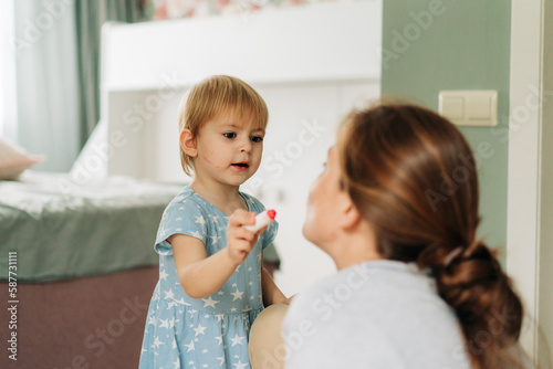 A little daughter makes a make-up for her mother and paints her lips with lipstick.