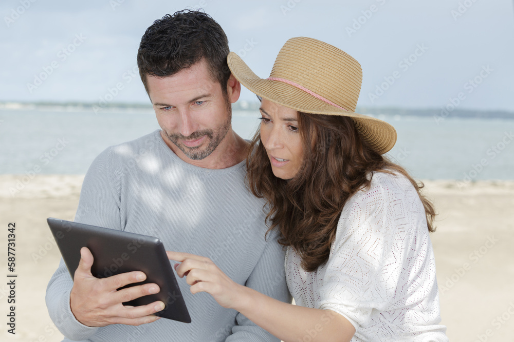 couple using tablet on the beach