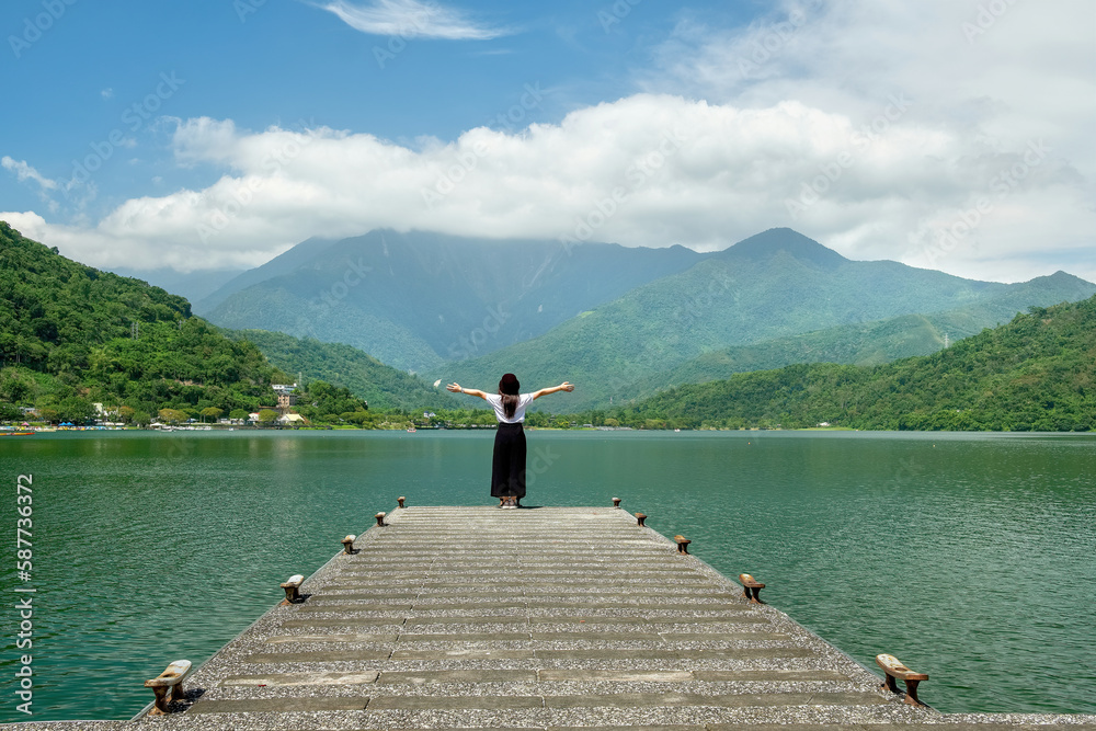 Asian woman standing on an empty pier looking at the view of the lake and mountains at Carp Lake, Taiwan