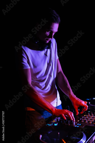 Cool young DJ playing music on party in night club. Night club disc jockey mixing musical tracks with sound mixer and vinyl turntables