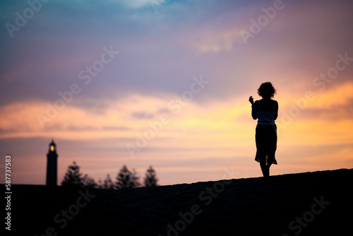 Obraz na płótnie Stunning view of a silhouette of a person walking on some sand dunes at sunset with the Maspalomas lighthouse in the distance. Gran Canaria, Canary Islands w salonie