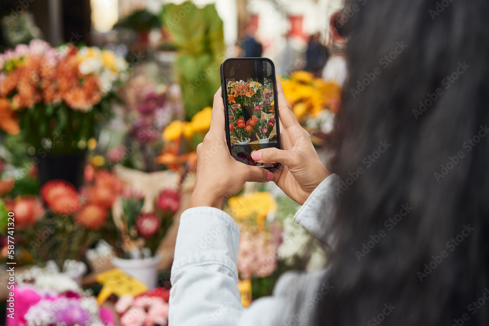 Young Latina woman capturing the vibrant beauty of flowers at a street vendor's stall with her mobile phone.