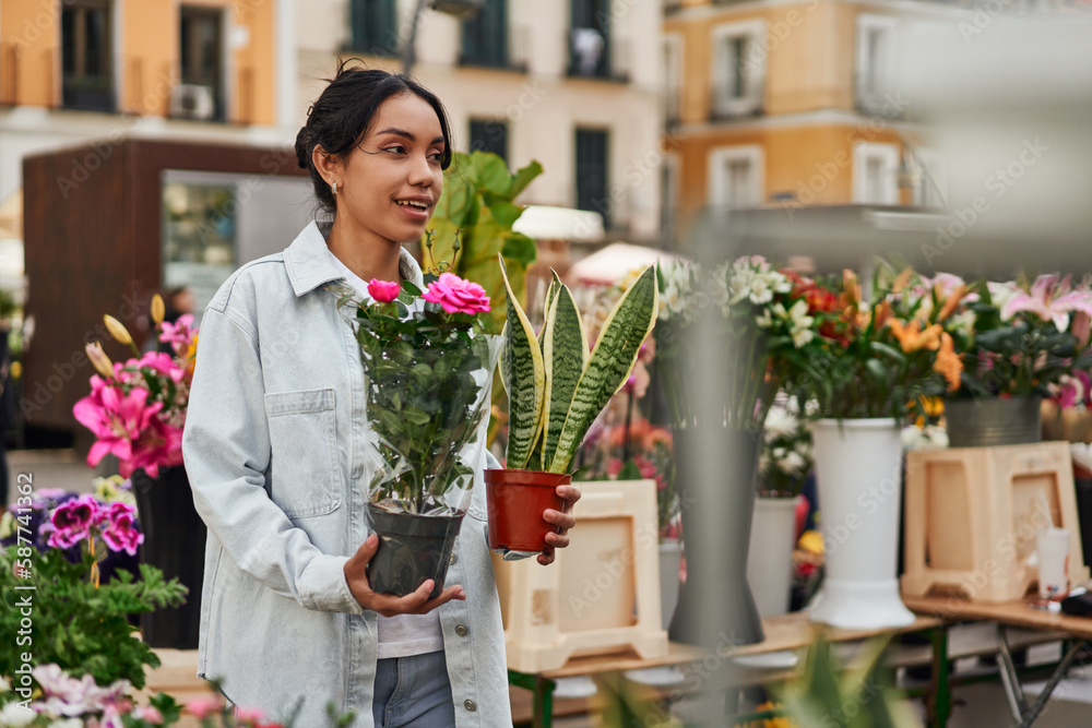 Young Latina woman smiling while purchasing plants from a street vendor's stall, adding beauty to her surroundings.