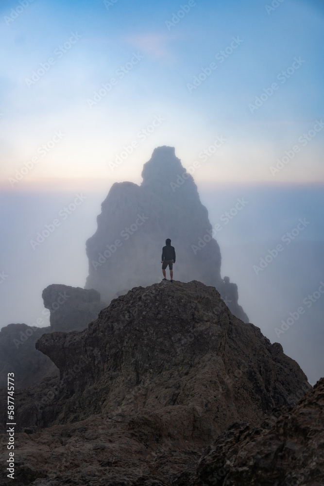 Stunning view of a person on the top of a rocky formation during a beautiful sunrise. Pico de las Nieves, Gran Canaria, Canary Islands, Spain.