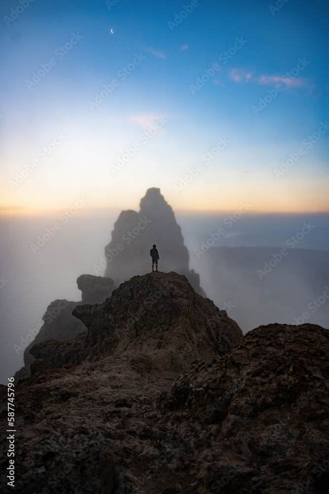 Stunning view of a person on the top of a rocky formation during a beautiful sunrise. Pico de las Nieves, Gran Canaria, Canary Islands, Spain.