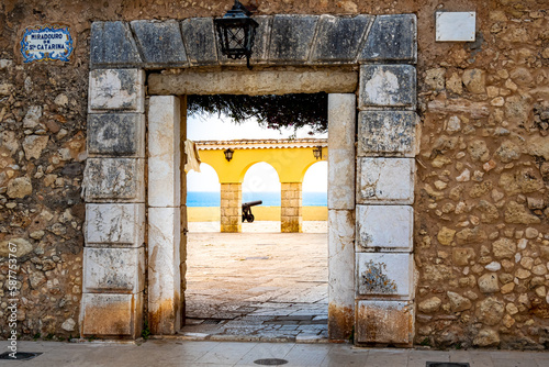 Through the entrance of viewpoint Miradouro de Santa Catarina in Portimão, visitors can behold a breathtaking view of the patio featuring an old cannon and the vast horizon of the Atlantic Ocean.