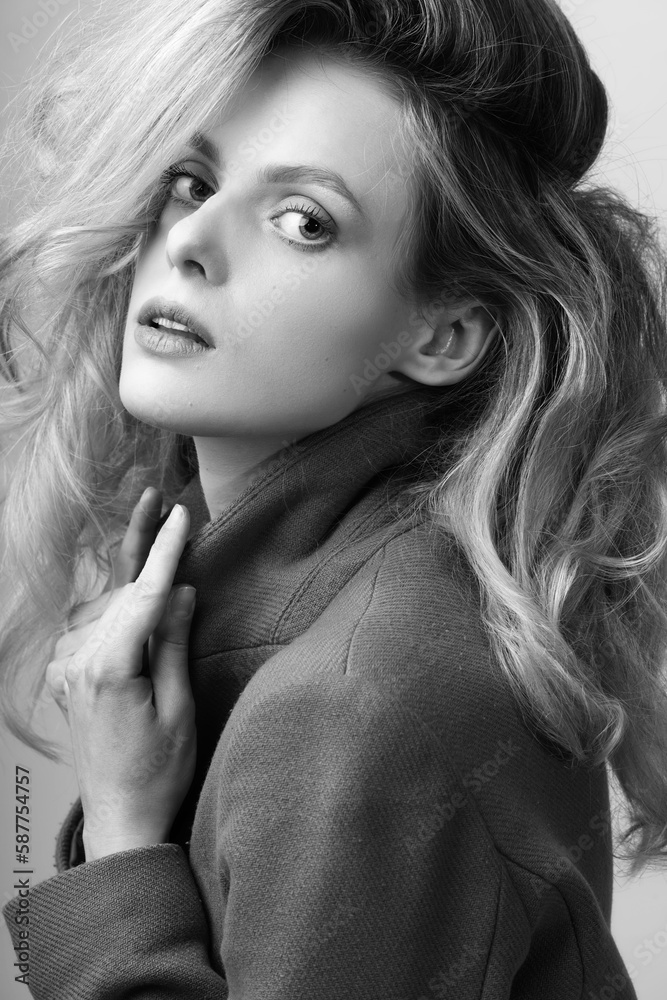 Naklejka premium Beauty concept. Beautiful blonde woman with big wavy hair close-up studio portrait. Model with make-up wearing garment coat and looking at camera with seductive look. Black and white image