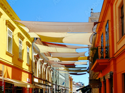 street awnings in perspective. colorful canvas sail shade and UV protection fabric suspended from exterior walls over the urban street in old city downtown area. sun protection. summer holiday concept