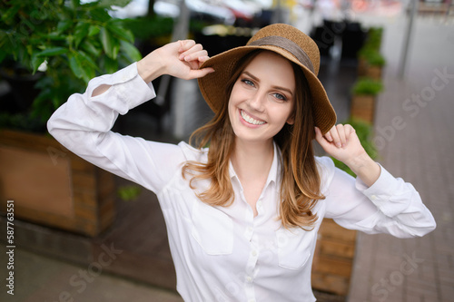 A young woman in a white shirt and hat looks at the camera, smiles.Portrait of a beautiful graceful woman.  © GRON777