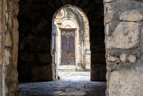 Mysterious old stone archway leading to the entrance of the Motsameta monastery in Imereti, Georgia, with old wooden carved doors with Saints David and Constantine images.