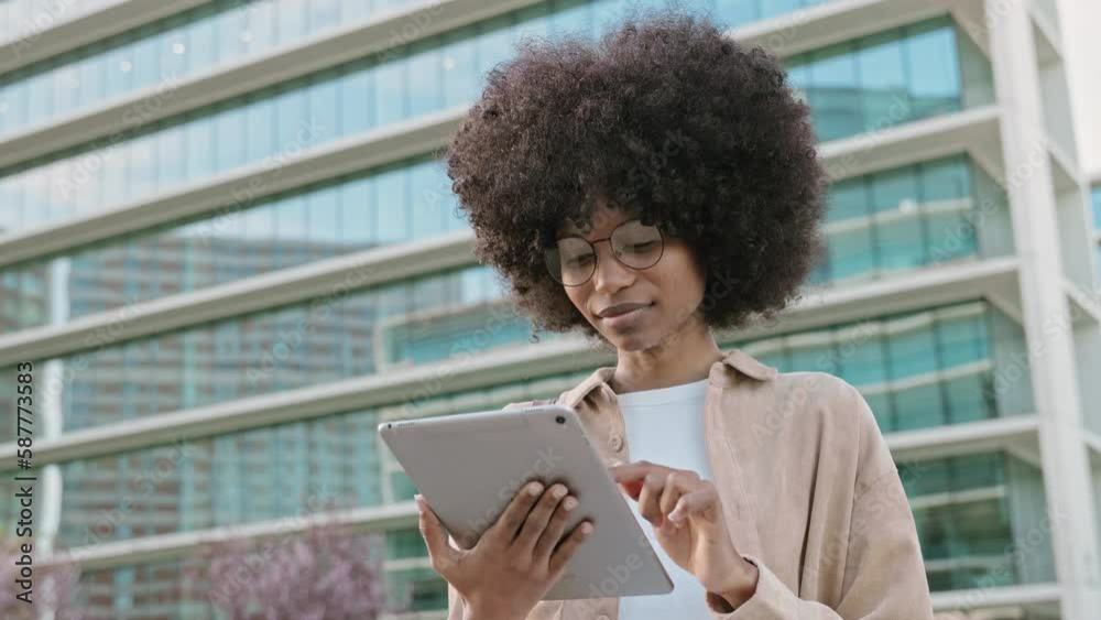 A young woman student using touchscreen of pc tablet standing in university campus. An African American cheerful female business freelancer entrepreneur using app project for online work outdoors. A young woman student using touchscreen of pc tablet standing in university campus. An African American cheerful female business freelancer entrepreneur using app project for online work outdoors.