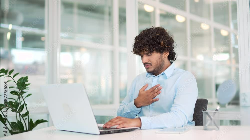 Sick young man suffering from heartburn while working on laptop while sitting at workplace at desk in modern office. A sad worker has digestive problems, he has acute gastritis or a stomach ulcer Sick young man suffering from heartburn while working on laptop while sitting at workplace at desk in modern office. A sad worker has digestive problems, he has acute gastritis or a stomach ulcer