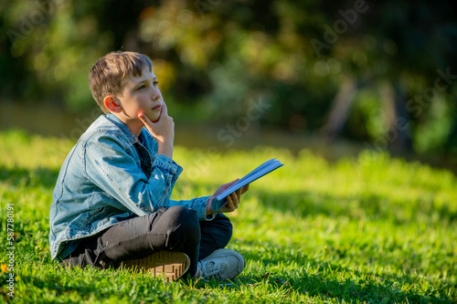 Tableau sur toile Student with a textbook in his hands is sitting on a green lawn in a park