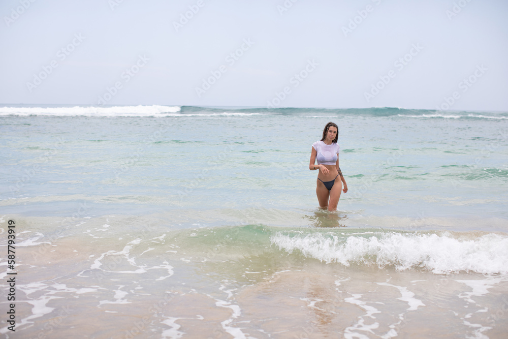 Beautiful young woman in a white cropped t-shirt comes out of the ocean.
