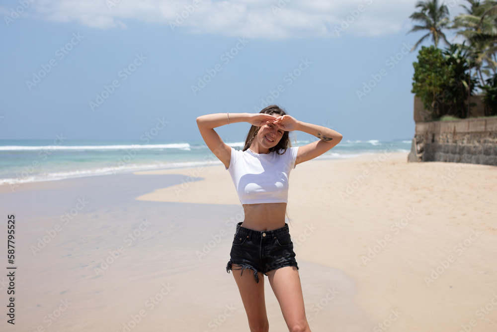 Attractive woman in a white cropped t-shirt walking along a beautiful beach. Attractive woman in a white cropped t-shirt walking along a beautiful beach.