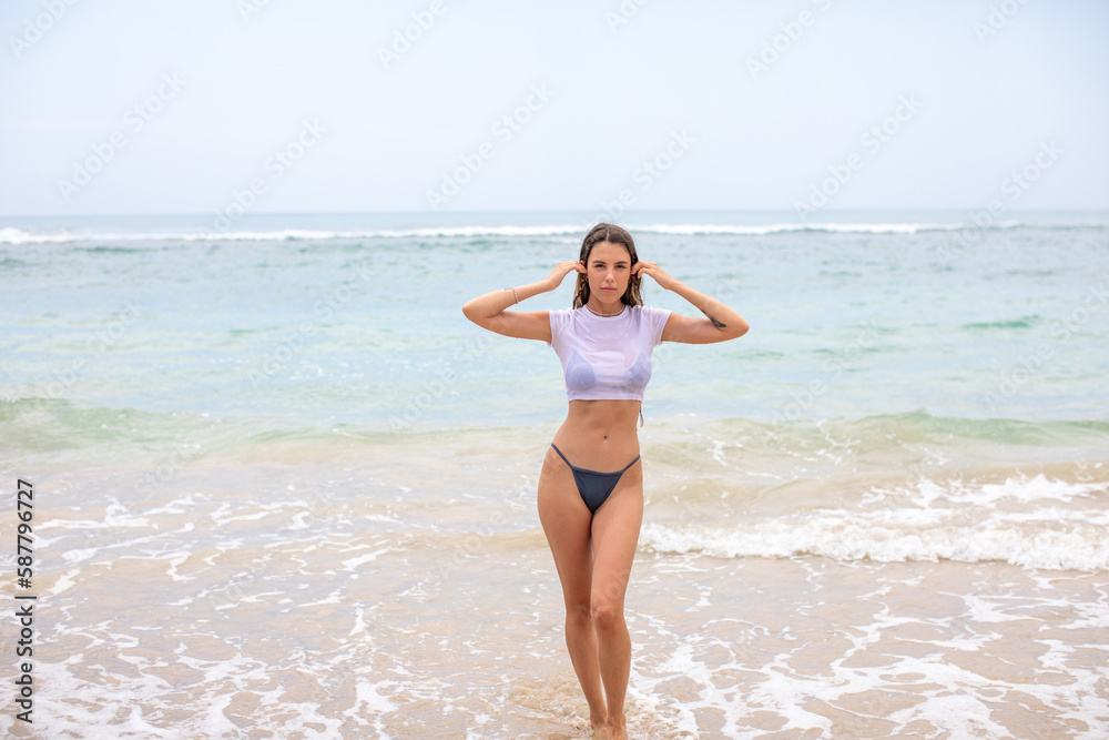 Beautiful young woman in a white cropped t-shirt comes out of the ocean. Beautiful young woman in a white cropped t-shirt comes out of the ocean.