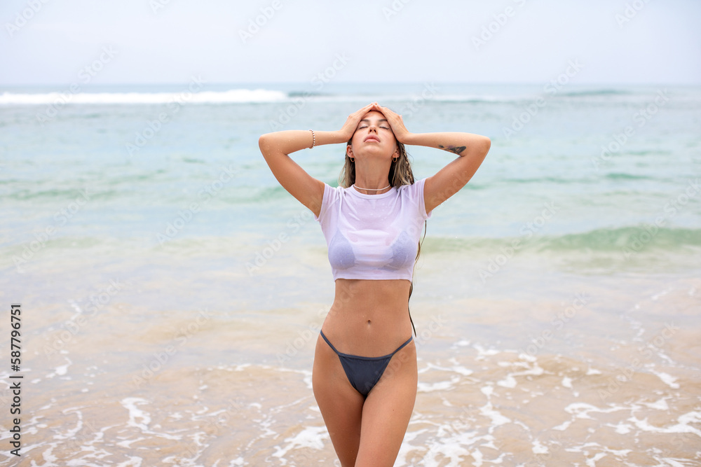 Beautiful young woman in a white cropped t-shirt comes out of the ocean. Beautiful young woman in a white cropped t-shirt comes out of the ocean.