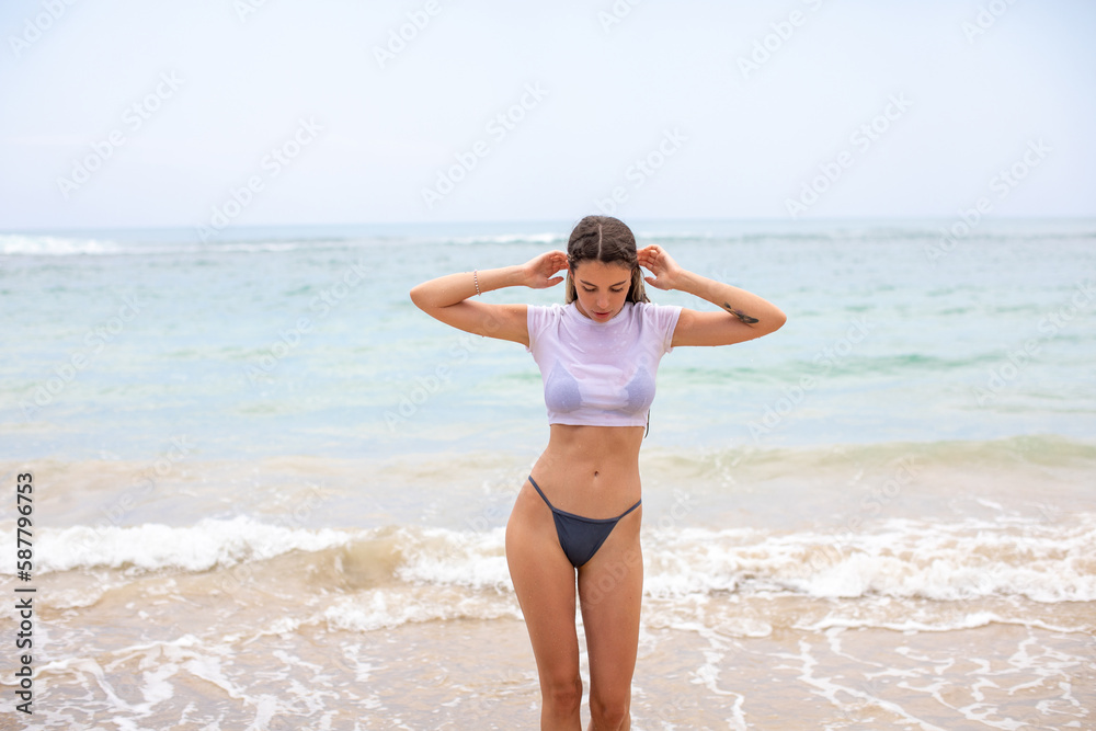 Beautiful young woman in a white cropped t-shirt comes out of the ocean. Beautiful young woman in a white cropped t-shirt comes out of the ocean.