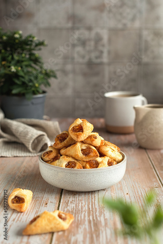 Close-up of a child's hand taking homemade puff pastry with jam from a ceramic bowl on a wooden table. Homemade cookies with jam in a ceramic bowl on a wooden table.