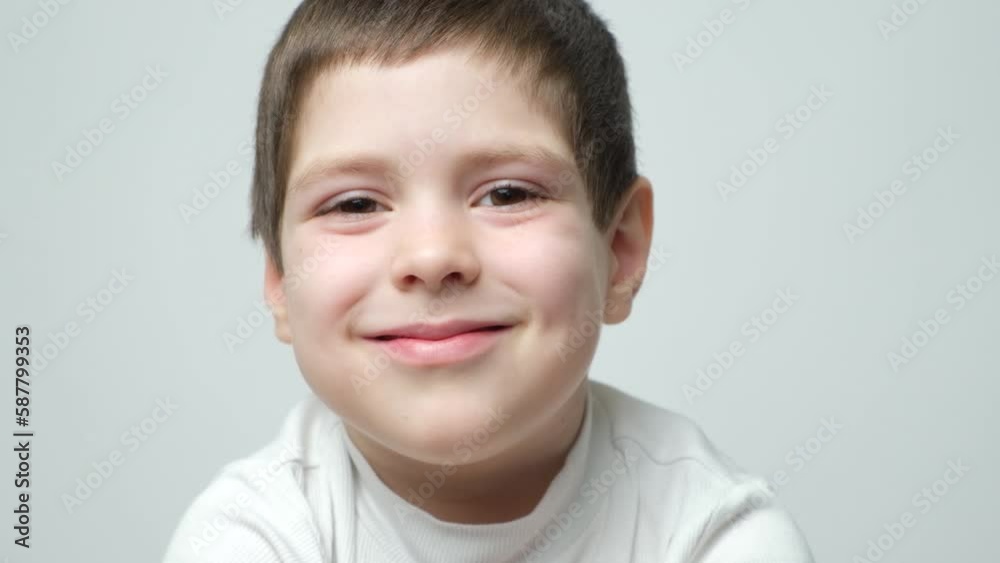 Handsome smart 5 year old brunette boy smiling and staring into the camera, blinking, opening and closing his eyes on a white background Handsome smart 5 year old brunette boy smiling and staring into the camera, blinking, opening and closing his eyes on a white background