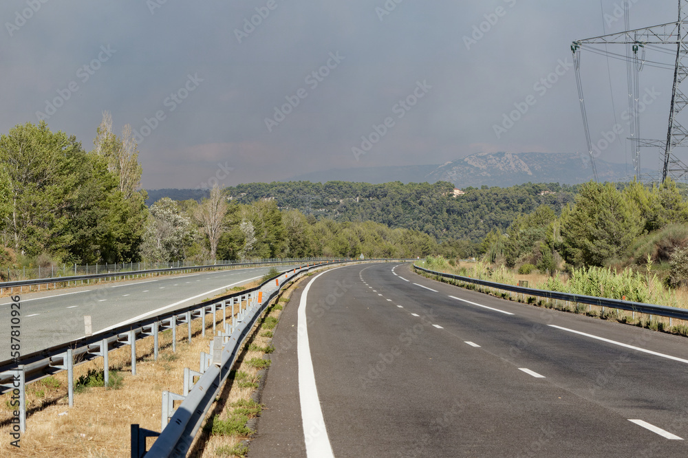 virage d'autoroute sans voiture avec présence d'un pylone électrique, et un ciel nuageux du fait d'incendie 