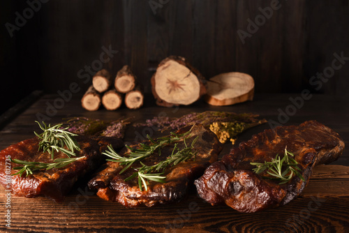 Dried Processed Beef Jerky with herbs and spices on wooden board against black background.