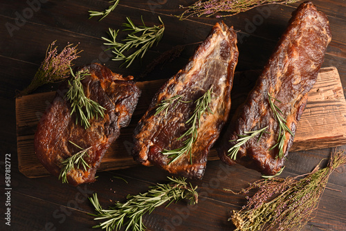 Dried Processed Beef Jerky with herbs and spices on wooden board against black background.