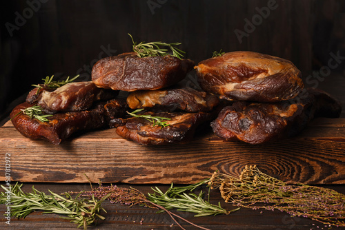 Dried Processed Beef Jerky with herbs and spices on wooden board against black background.