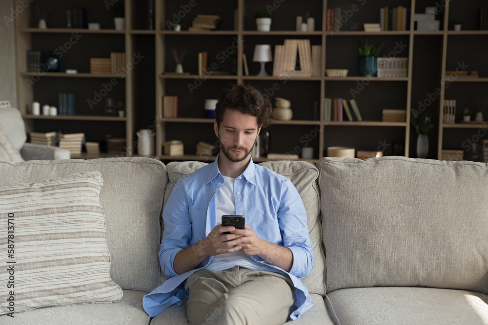 Fototapeta premium Serious young smartphone user man texting message, chatting, typing, using ecommerce application for online shopping, virtual service, software, making payment on Internet