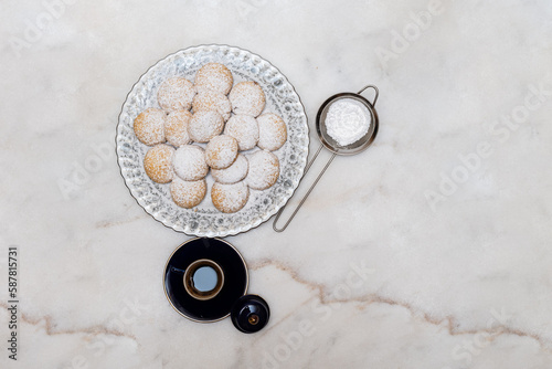 Kahk with sugar sprinkled on top in a rounded china plate and a cup of Turkish coffee on white marble background, (Kahk is a traditional cookies after Ramadan for eid)
