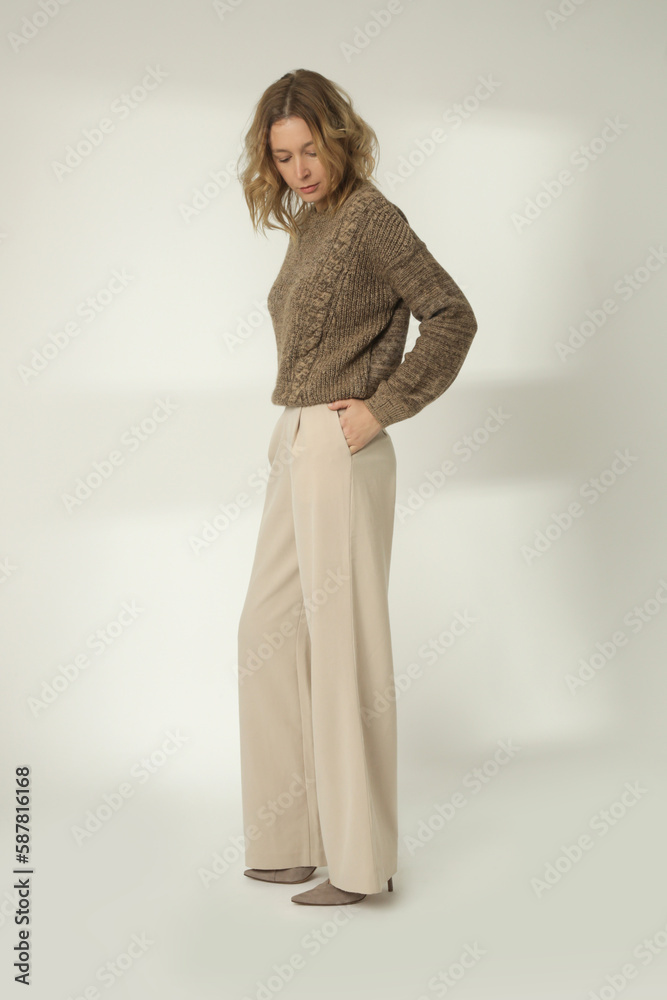 Fashion portrait of young woman in brown winter sweater and beige wide pants on the white background Fashion portrait of young woman in brown winter sweater and beige wide pants on the white background