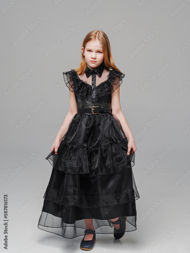 Fototapeta premium cute blonde teen girl in a black long curvy dress on a gray background. 