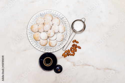 Kahk with sugar sprinkled on top in a rounded china plate and a cup of Turkish coffee on white marble background, (Kahk is a traditional cookies after Ramadan for eid)
