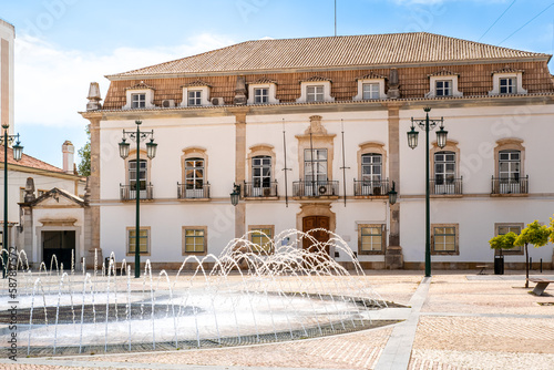 On a sunny spring day in May, the round water fountain on Praça 1 de Maio square stands in front of the impressive Portimão City Hall, providing a serene and tranquil backdrop to the downtown area.