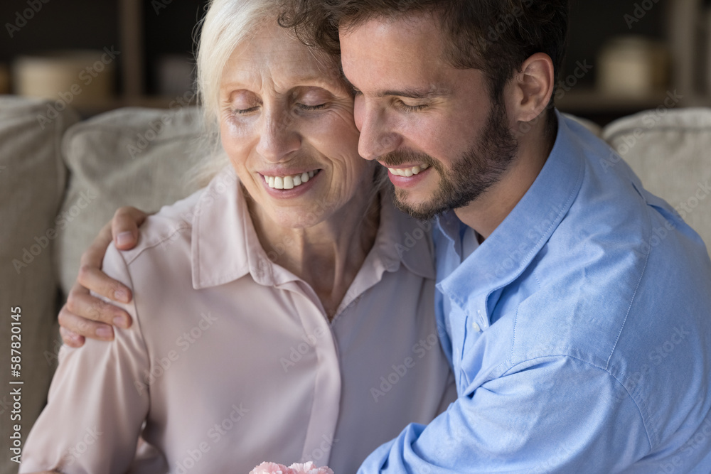 Peaceful cheerful handsome adult guy embracing happy older senior mom with love, affection, tenderness, gratitude, smiling with closed eyes, enjoying family relationships, leisure Peaceful cheerful handsome adult guy embracing happy older senior mom with love, affection, tenderness, gratitude, smiling with closed eyes, enjoying family relationships, leisure