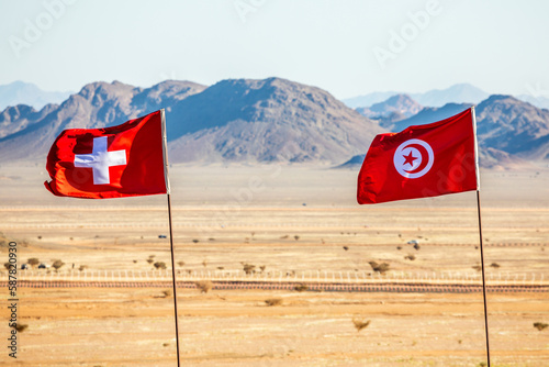 Tunisean and Switzerland flags waving togetner on the wind in Saudi Arabian desert, Al Ula, Saudi Arabia photo