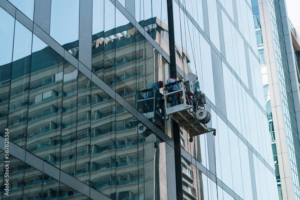trabajador en alturas limpiando vidrios en un edificio en el centro en una grúa mecánica con cuerdas y protección.