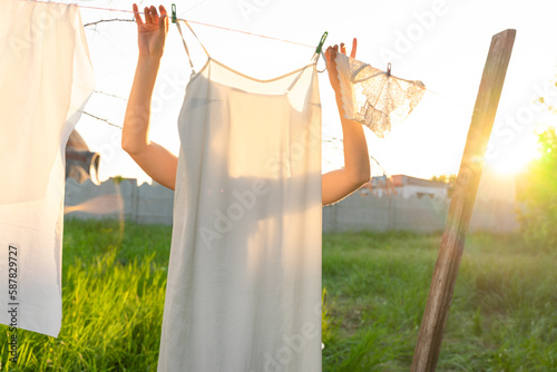 Young woman hanging laundry outdoors. Beautiful girl working in countryside.Cute blonde girl in dress washing white clothes in metal basin in backyard. village girl in a headscarf